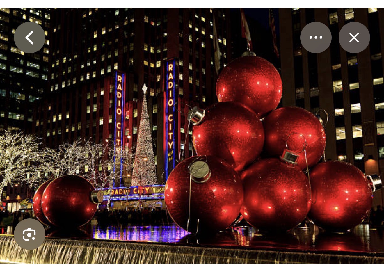 Giant red Christmas ornaments in front of the Radio City Music Hall marquee at night in Rockefeller Center